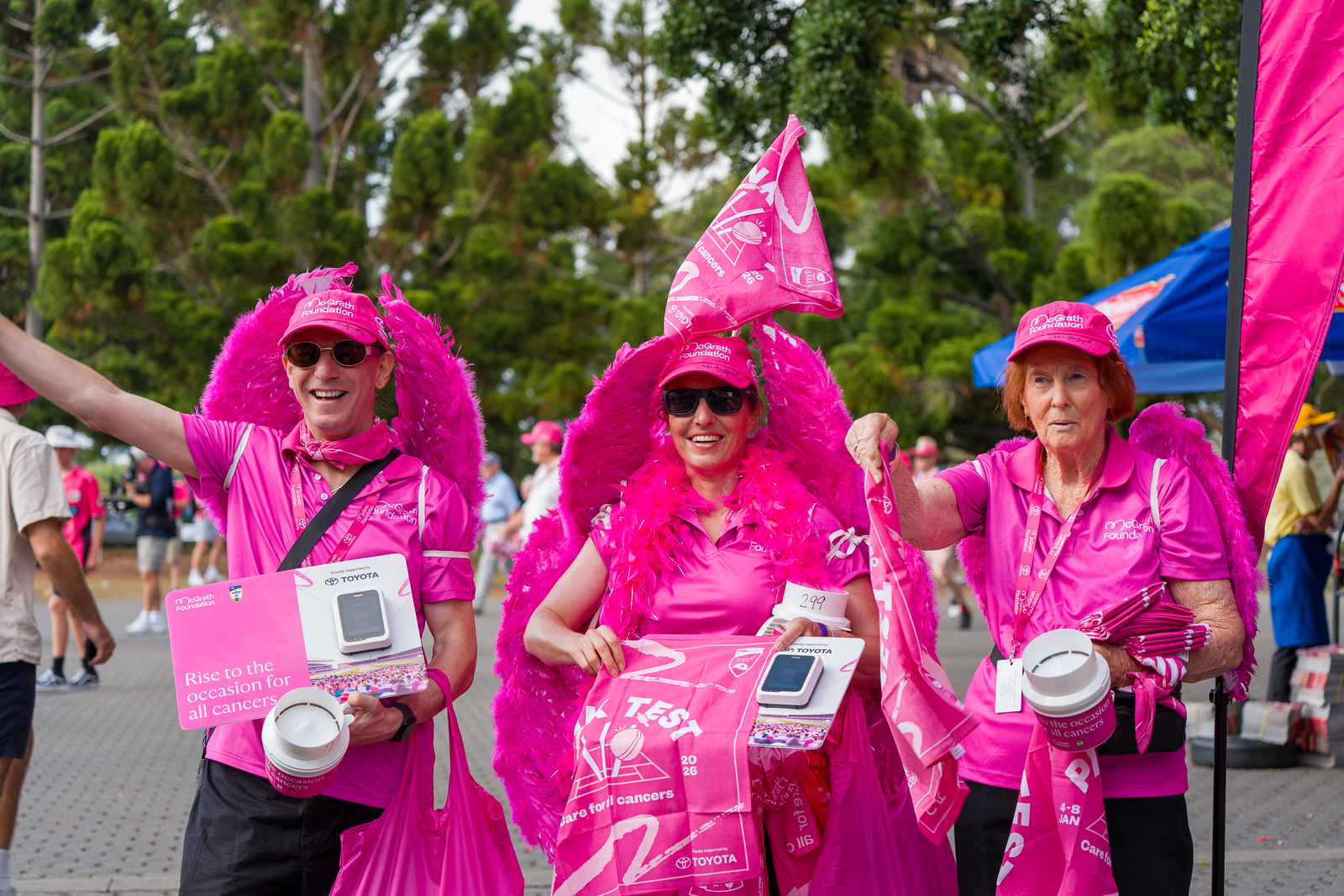Three volunteers in pink with feather wings and donation buckets raise funds at the Pink Test..