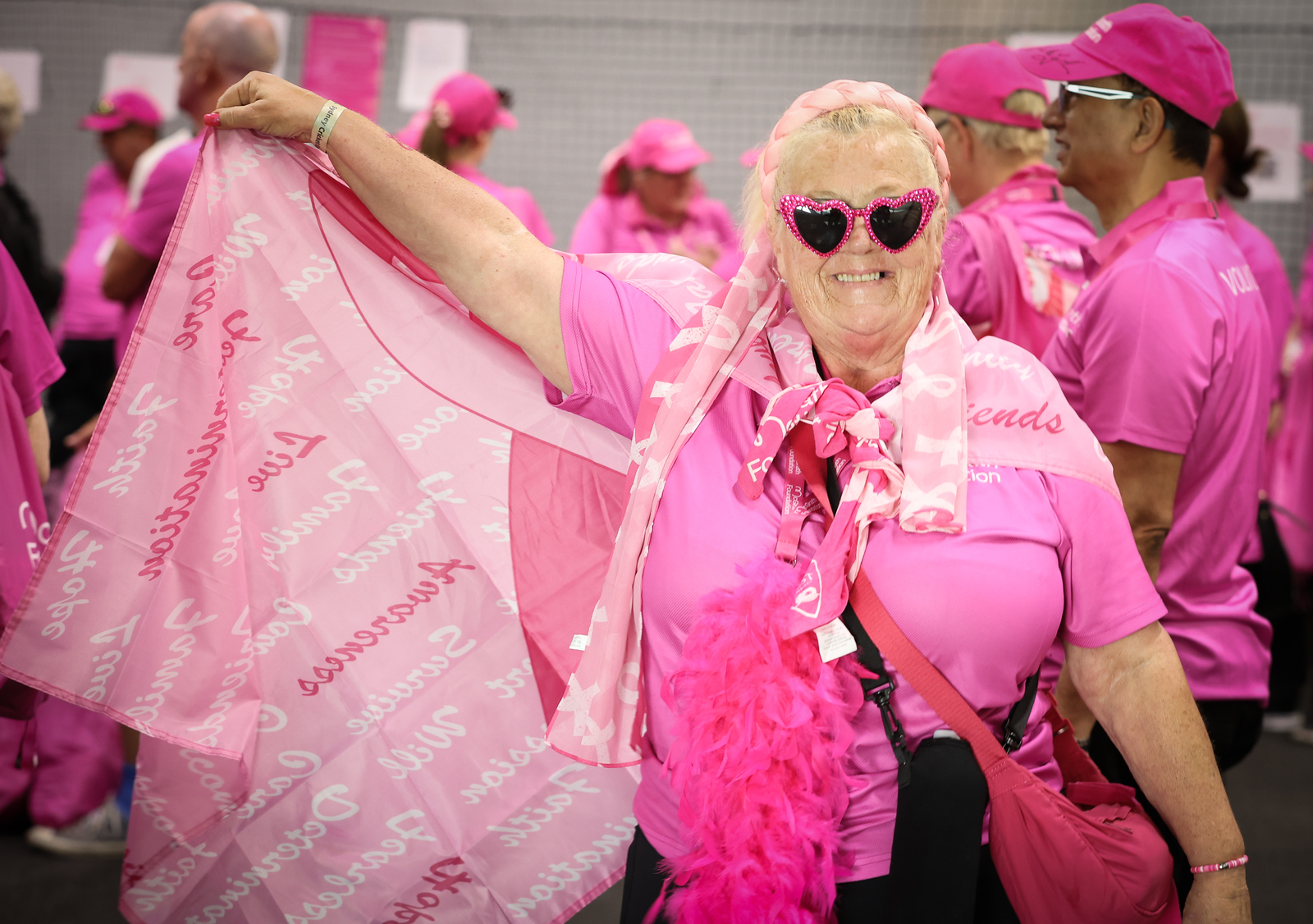 Volunteer in pink wearing heart-shaped sunglasses holds up a pink scarf at the Pink Test.