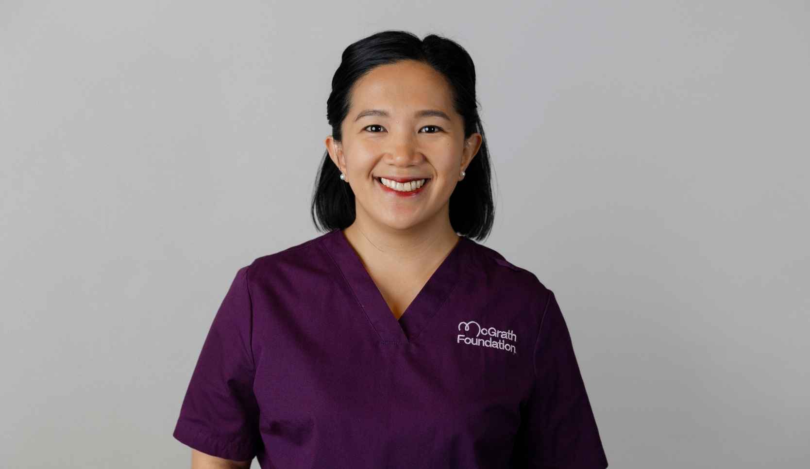 Headshot of a smiling woman with dark hair wearing purple McGrath Foundation scrubs