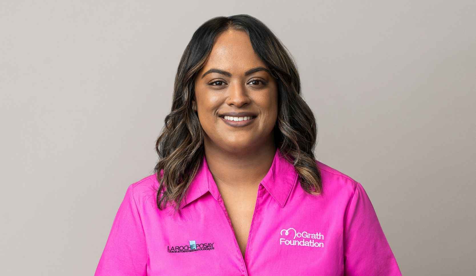 Headshot of a smiling woman with long dark hair wearing a pink McGrath Foundation shirt with a La Roche-Posay logo
