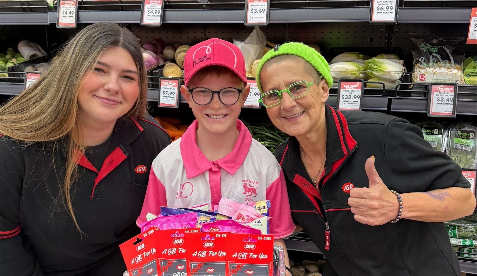Owen poses with IGA staff in-store holding a fundraising display with IGA gift cards and lollies for a McGrath Foundation community fundraiser.