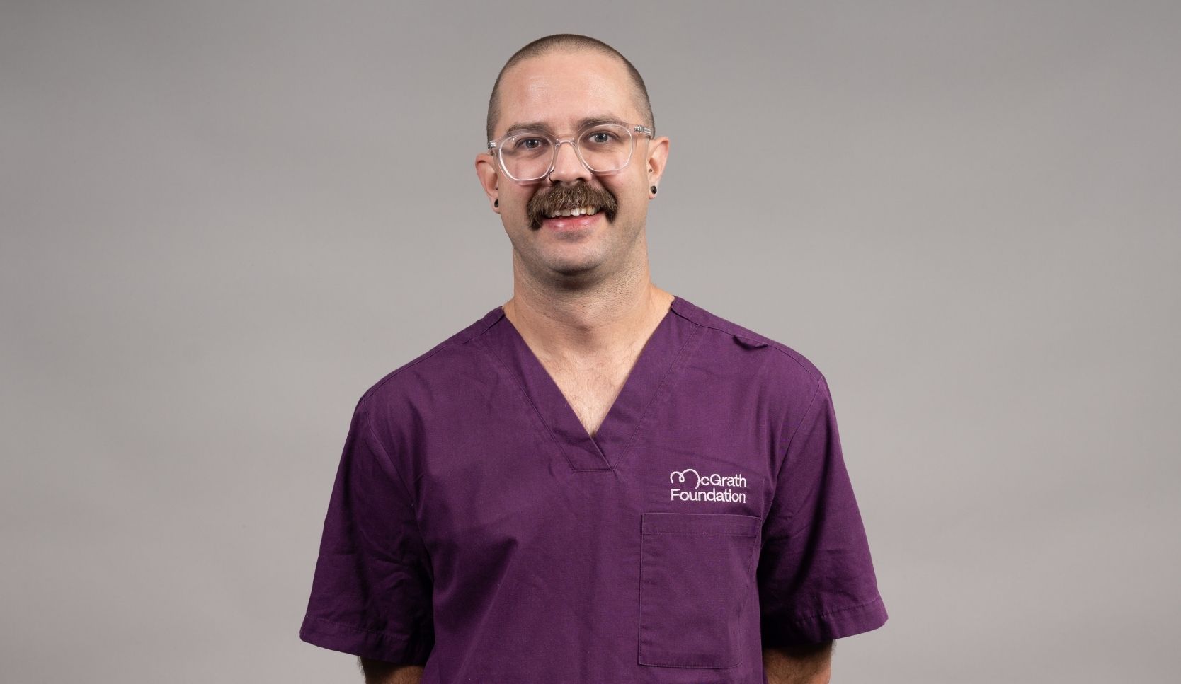 Portrait of a person wearing purple McGrath Foundation scrubs and glasses.