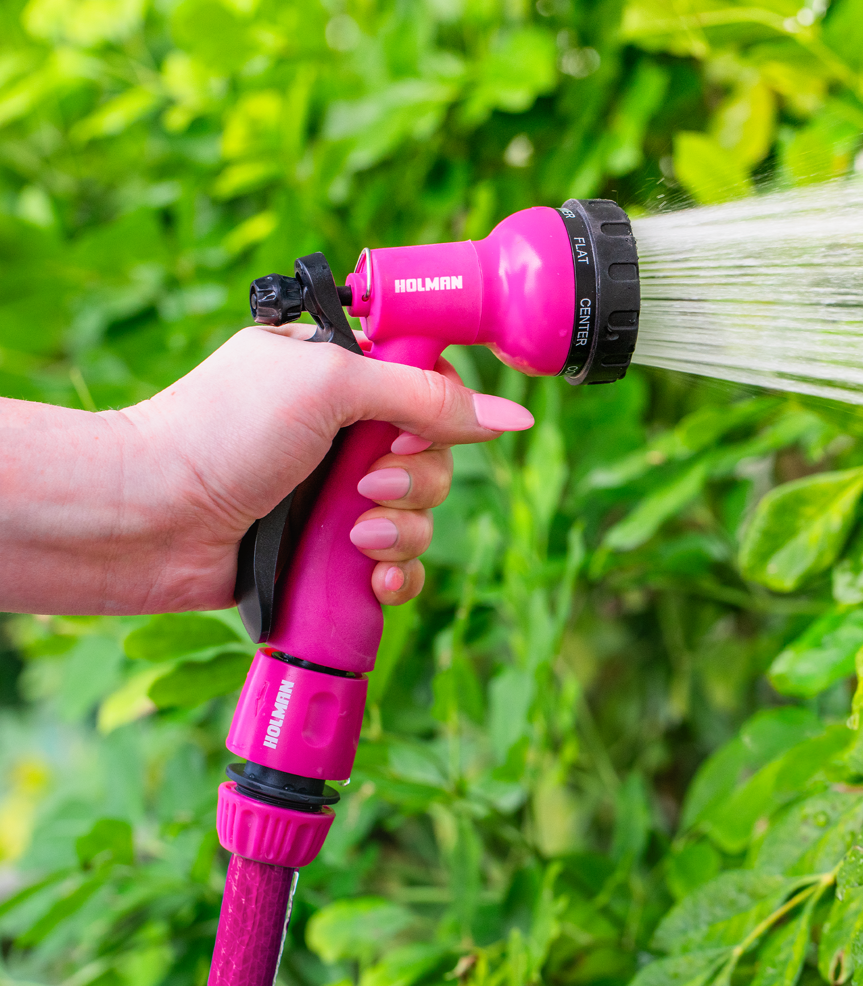 Hand holding a pink Holman spray gun hose attachment, watering plants.