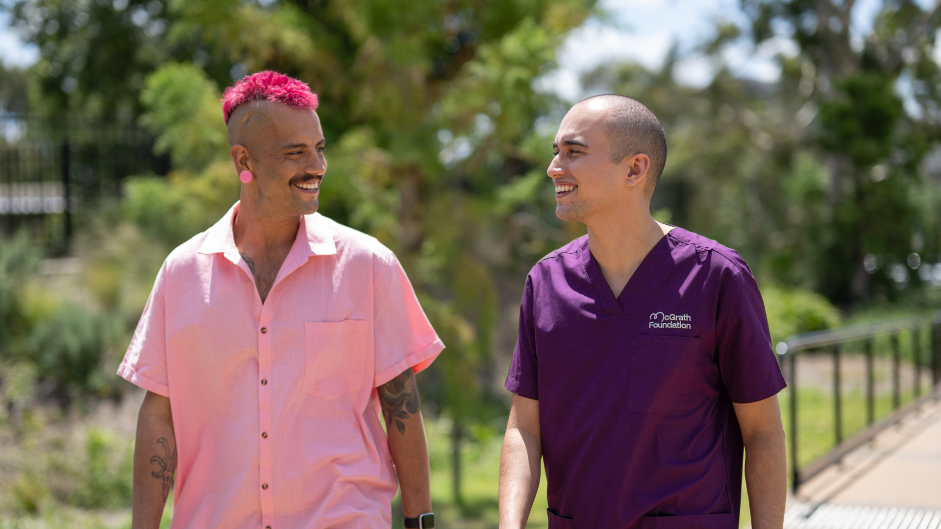 Male McGrath Cancer Care Nurse walking down a path outside with his male patient, looking at each other and smiling