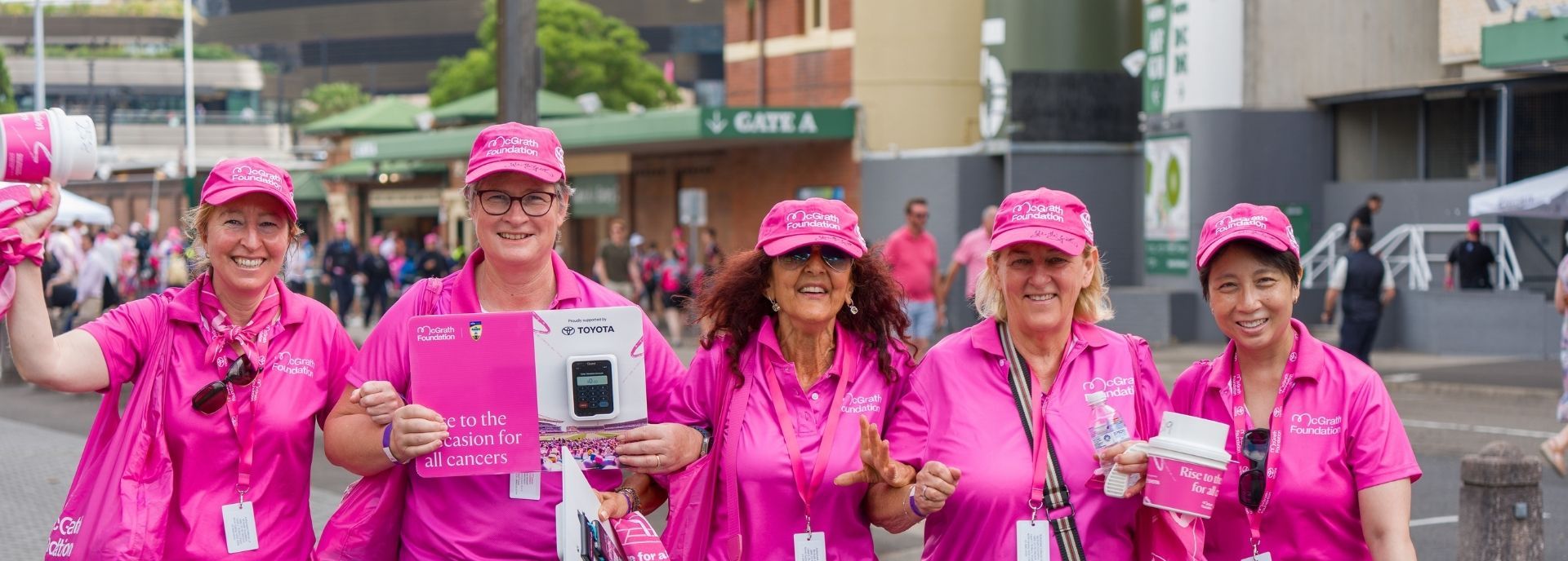 McGrath Foundation Pink Test volunteers walking together at a fundraising event, wearing pink uniforms and carrying event materials.