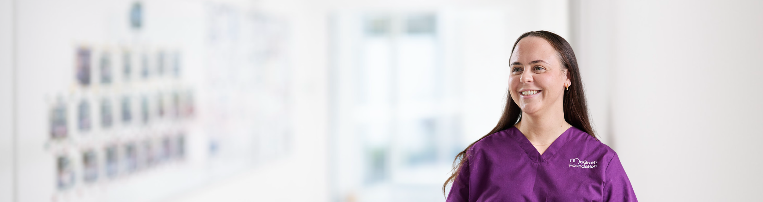 McGrath Cancer Care Nurse standing in the hallway of a medical facility looking away from the camera and smiling