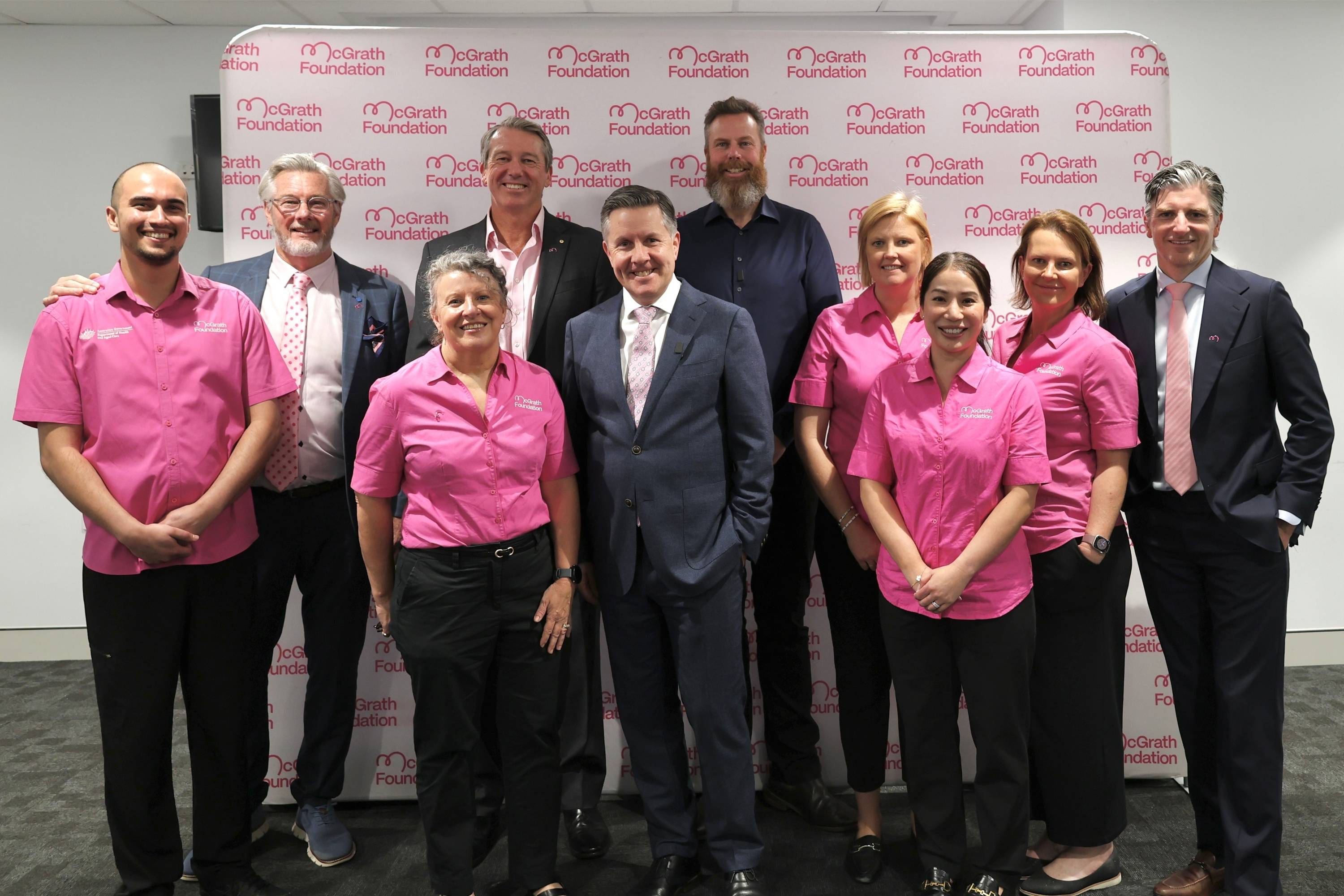 Group photo of McGrath Foundation representatives and government stakeholders standing in front of a McGrath Foundation media wall following the announcement of the expansion of McGrath Cancer Care Nurse support to include prostate cancer care.