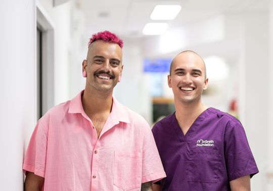 Matt and his McGrath Cancer Care Nurse, Jordan standing in the hallway of a health care facility looking at the camera and smiling