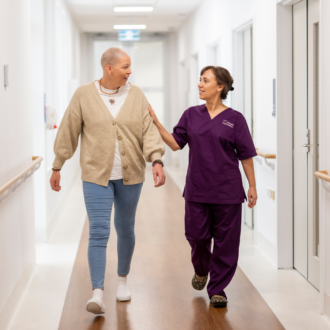 Female McGrath Foundation nurse with female cancer patient walking down a hospital hallway.