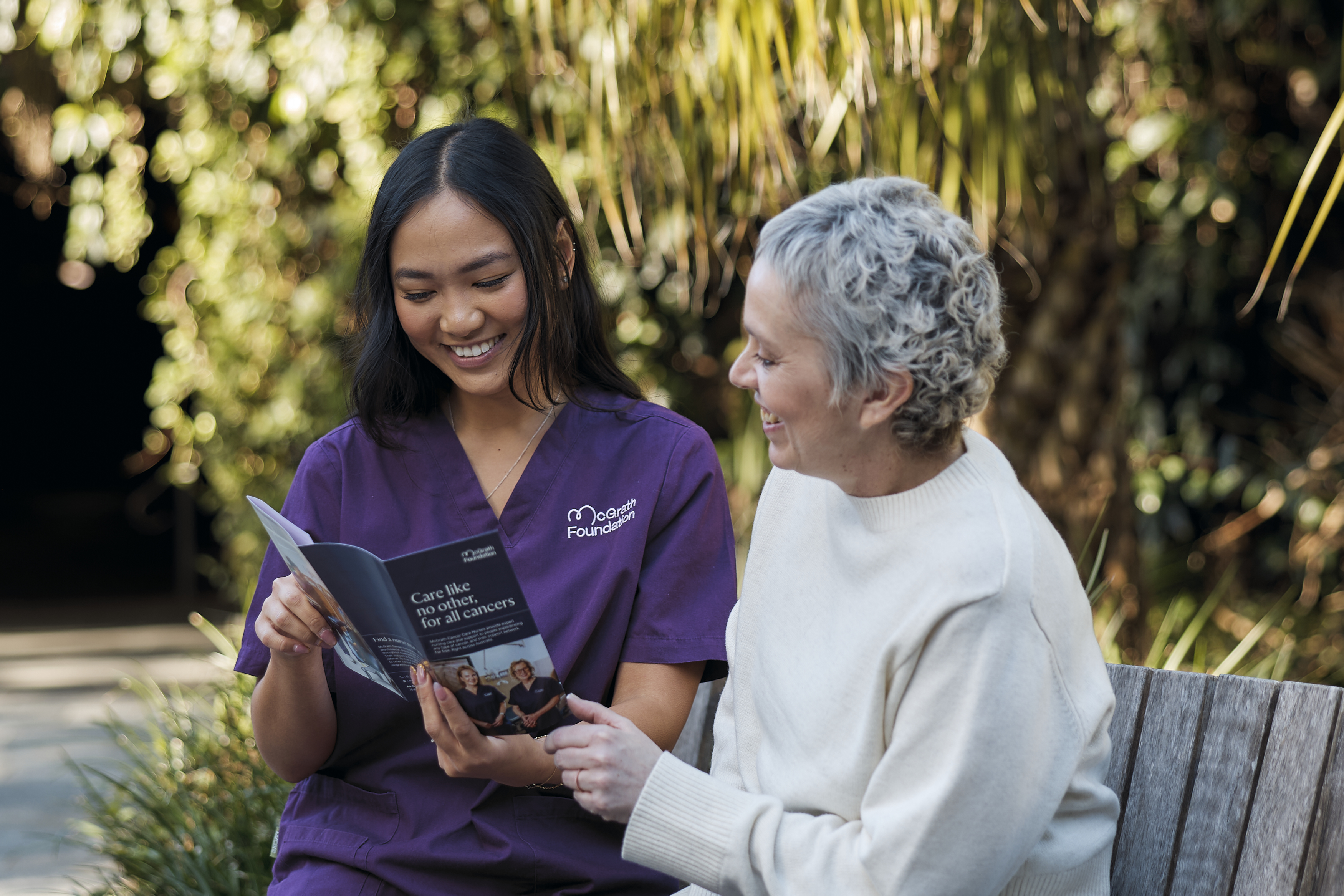 Smiling McGrath Foundation nurse showing McGrath Foundation brochure to older smiling woman.