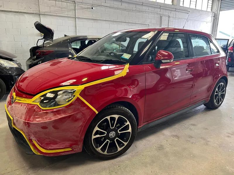 Red MG hatchback masked with tape for front panel and paint repair