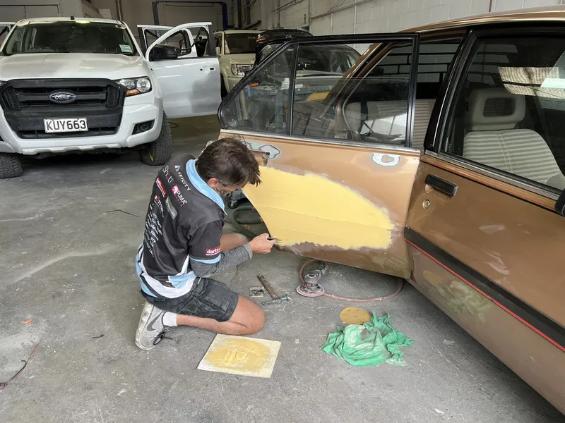 Technician sanding filler on the door of a bronze classic sedan