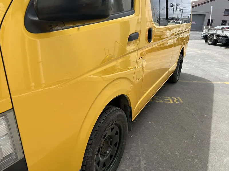 Crease damage along the side of a yellow Toyota Hiace before repair