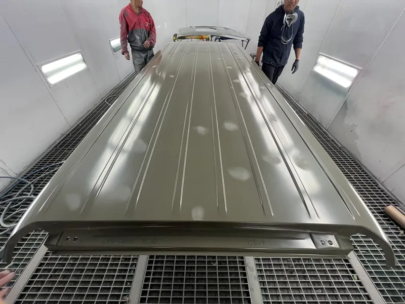 Two painters checking a freshly sprayed van roof panel in the spray booth