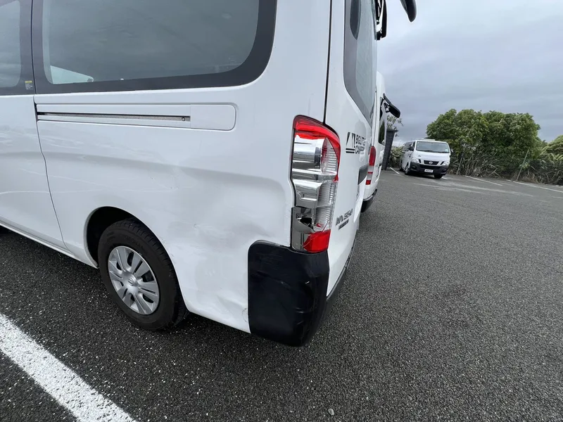 Dented rear quarter panel on a white van before repair