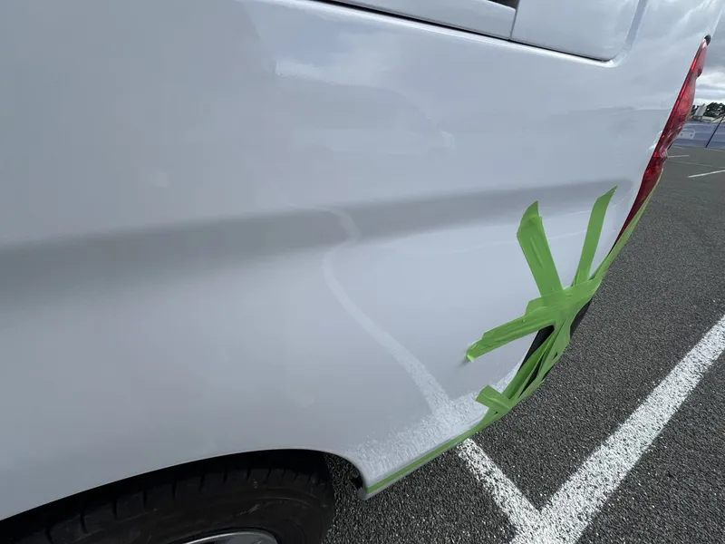 Crease damage marked with tape along the side of a white van