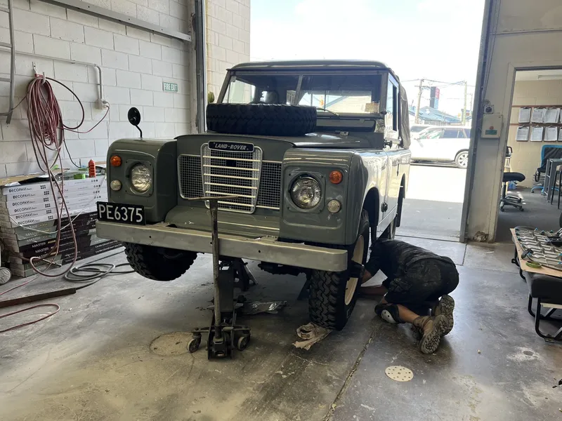 Classic Land Rover on a jack while a technician works on the front wheel