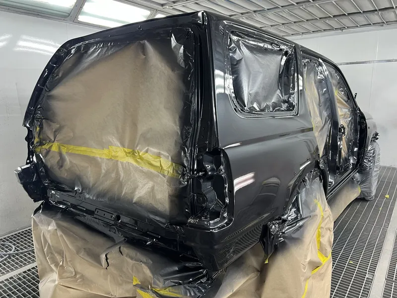 Black SUV masked with paper and tape in the spray booth before repainting