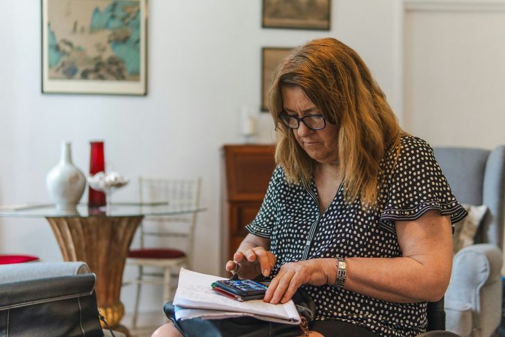 Woman using a calculator to check the fees on her loan paperwork at home