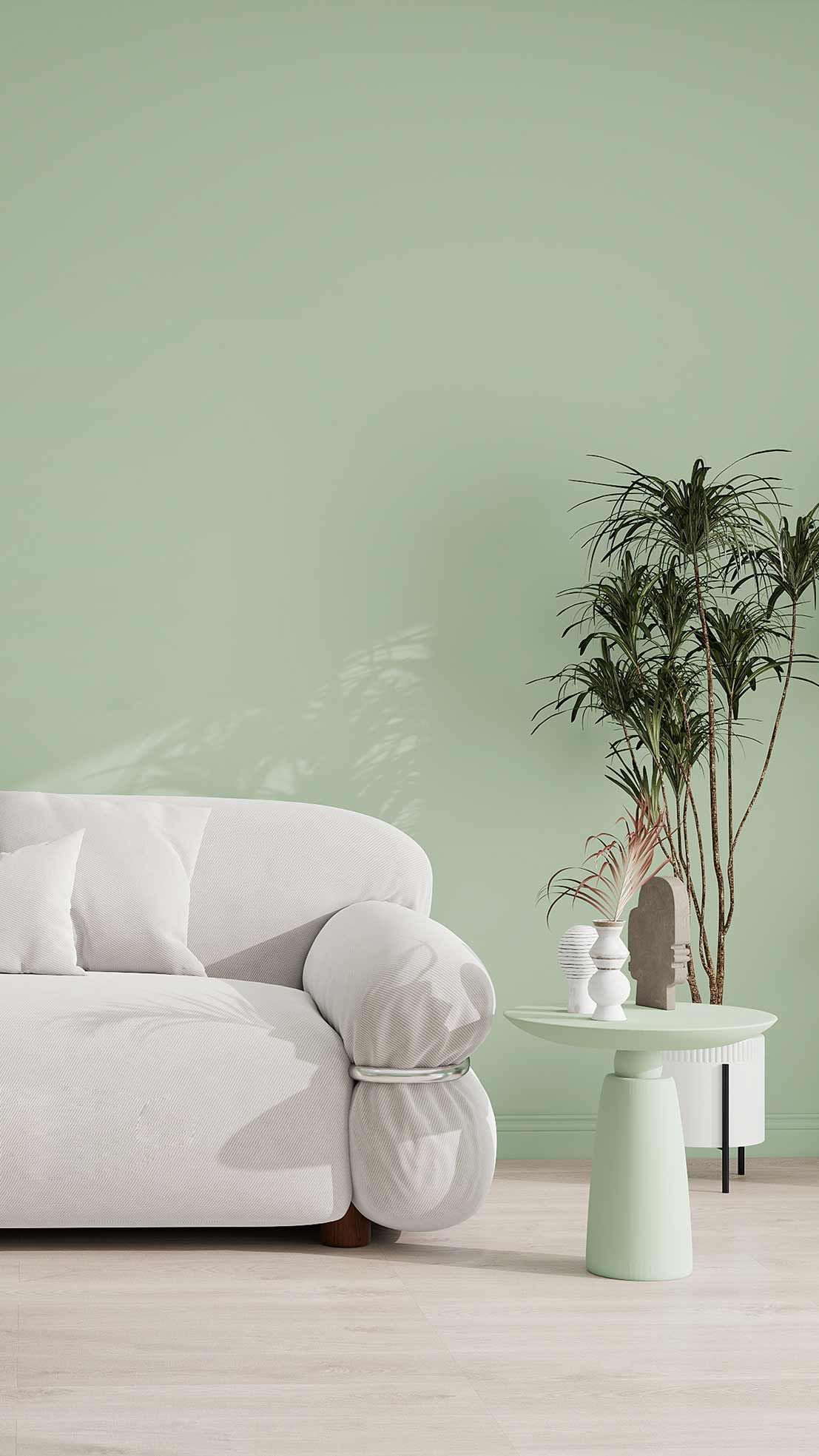 A cozy living room with a white sofa, gray cushions, a round coffee table, and shelves of potted plants against a light green wall.
