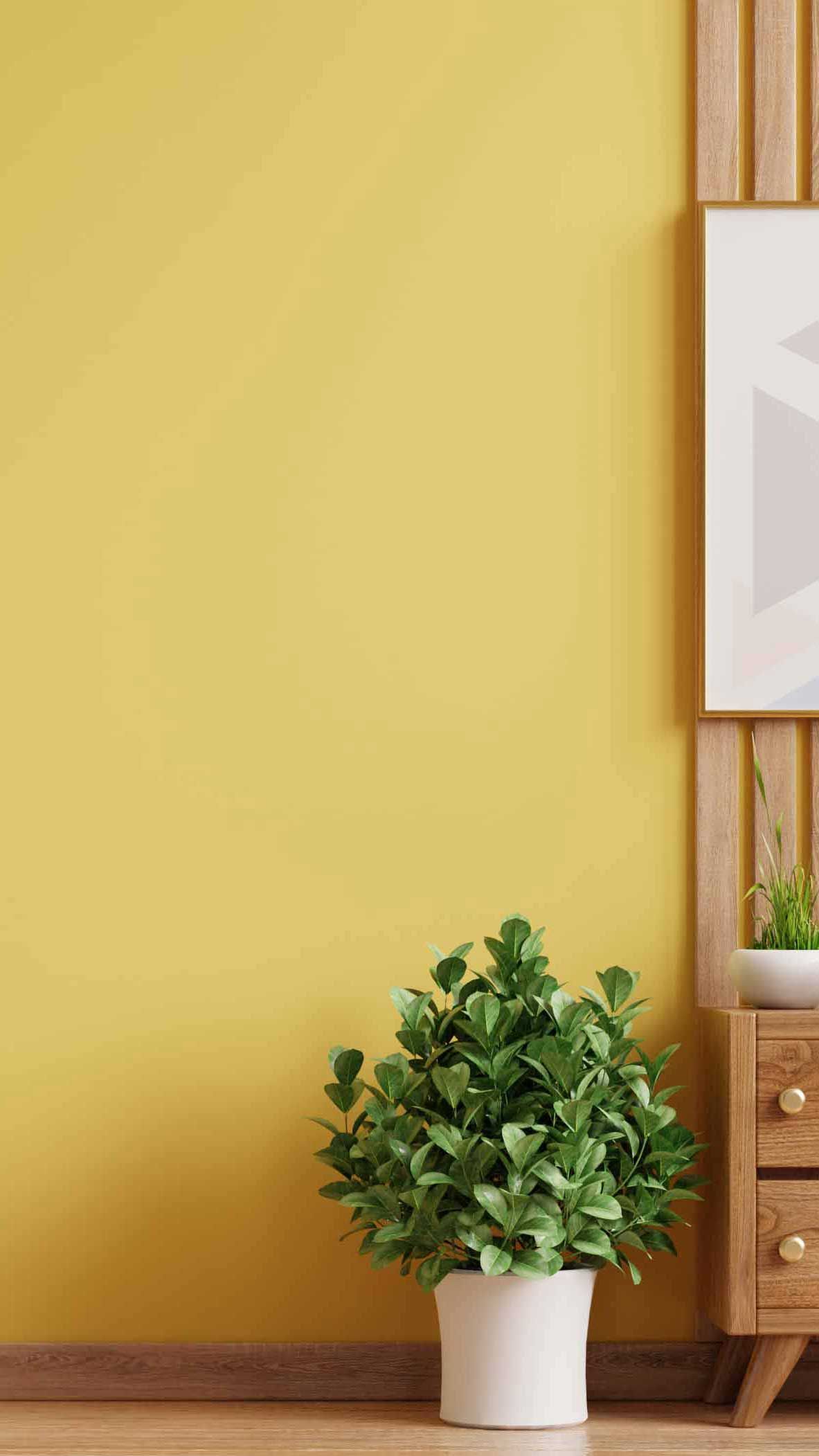 Minimalist interior with a geometric art piece on a wooden slat wall, yellow pendant light, and plants, against a matching yellow background.