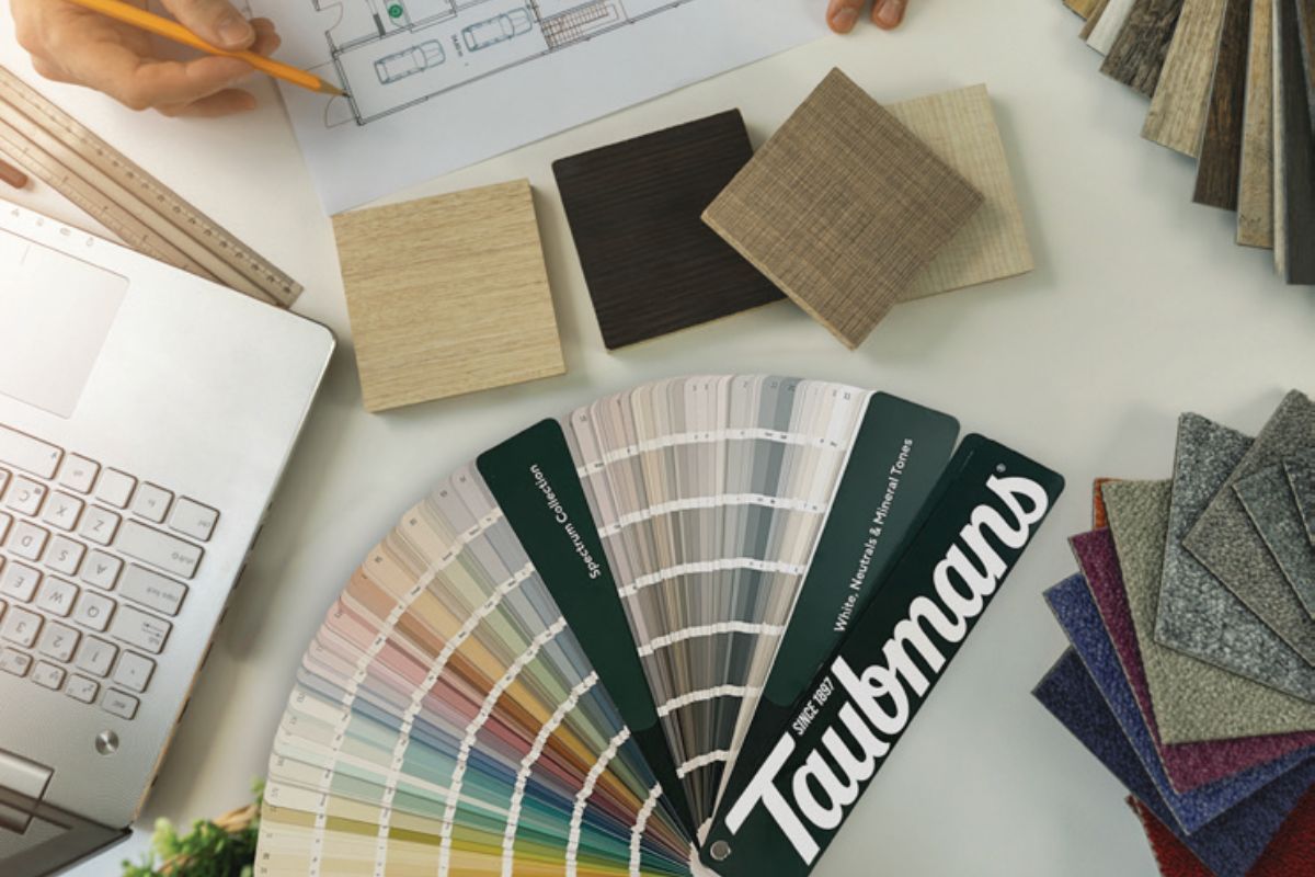 Taubmans fan deck placed on desk alongside timber flooring and carpet samples. A computer and architectural drawing can be seen.