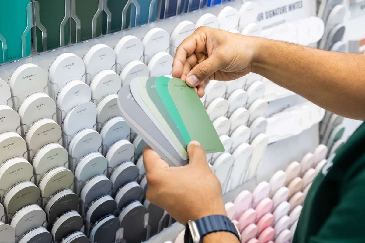 Person selecting paint swatches from a display, holding samples in green and gray shades.