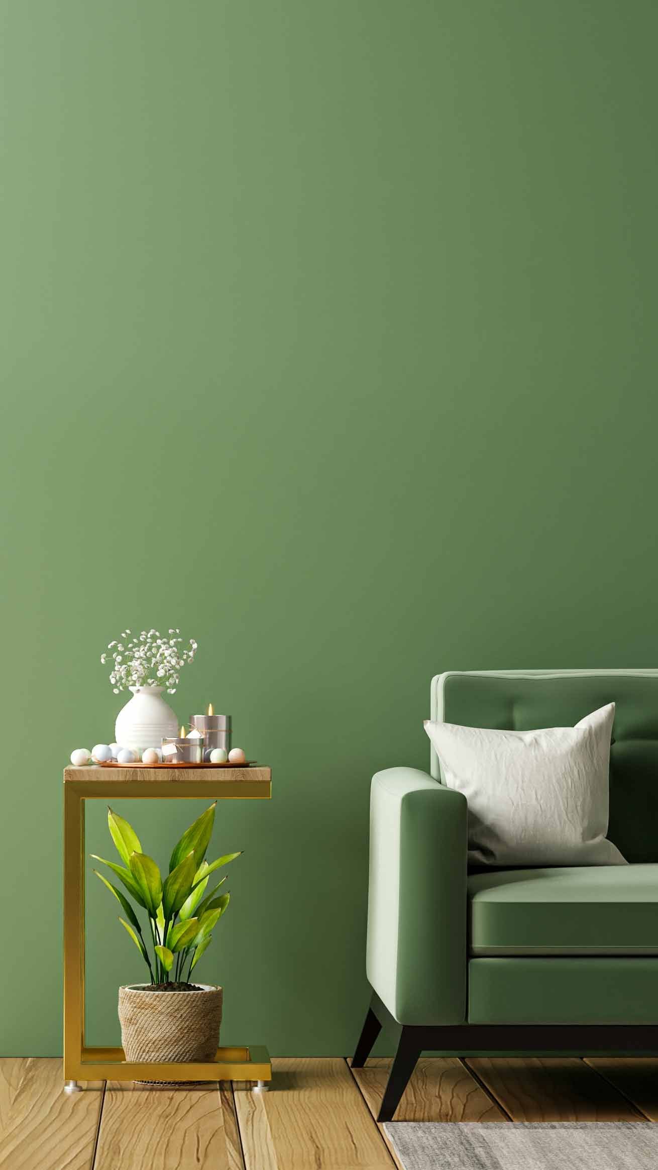A cozy living room with a green sofa, a white pillow, a side table with decor items, and a potted plant against a matching green wall.