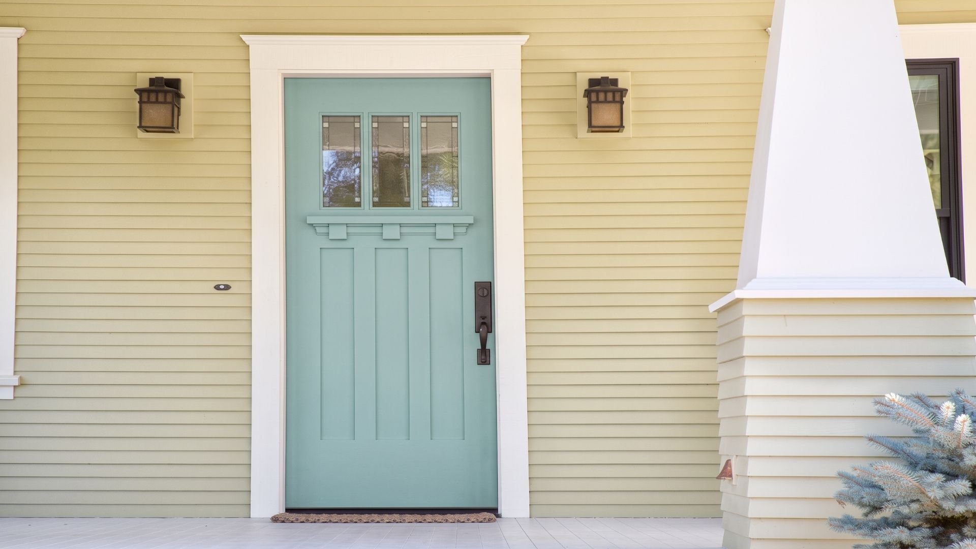 A light green front door with three glass panels set in a cream-colored wall, flanked by two wall lanterns.