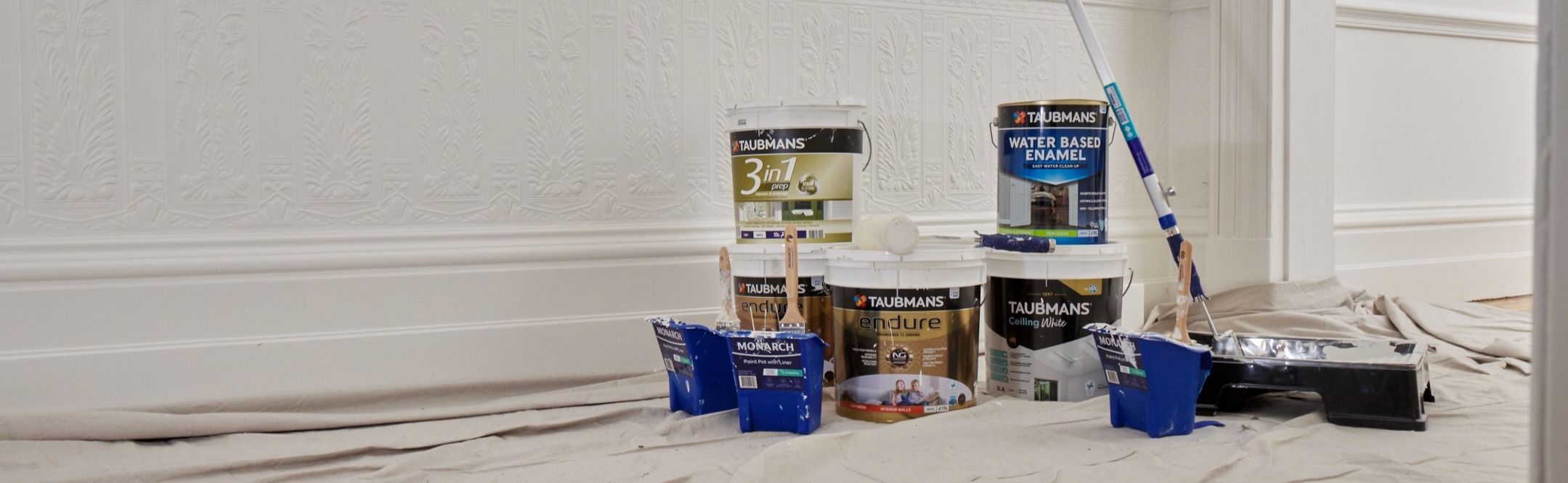 Buckets of paint and painting supplies are placed on a drop cloth in a room with ornate white walls.