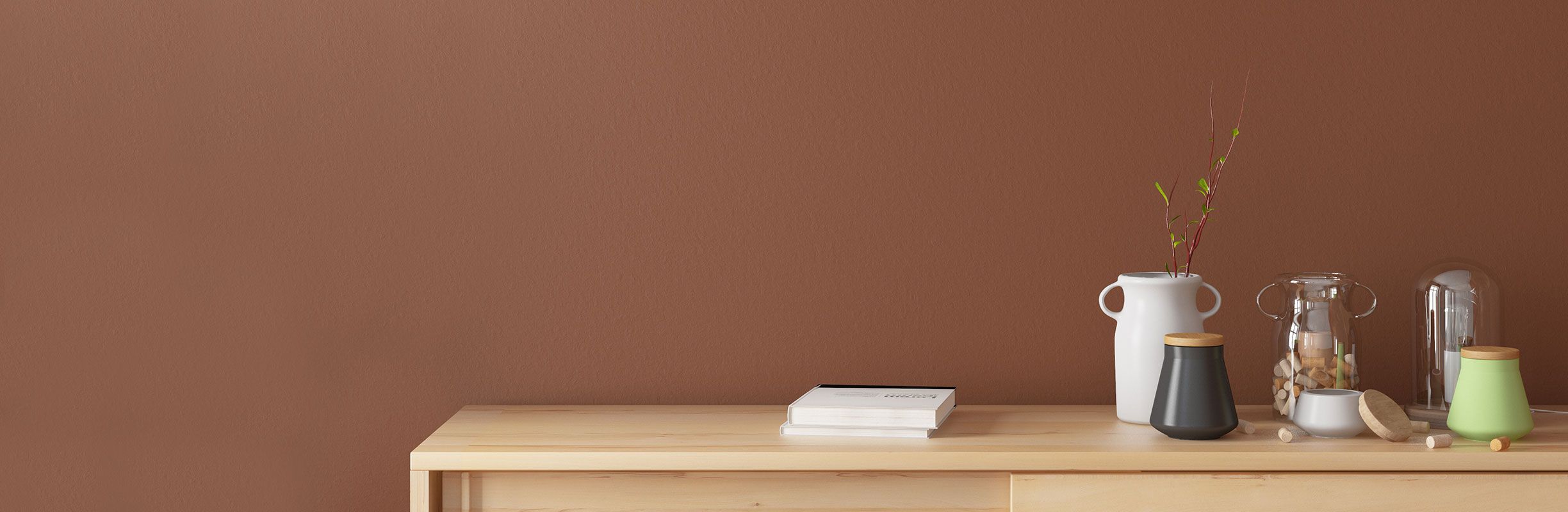 Minimalist wooden sideboard with books, vases, and a glass cloche against a brown wall.