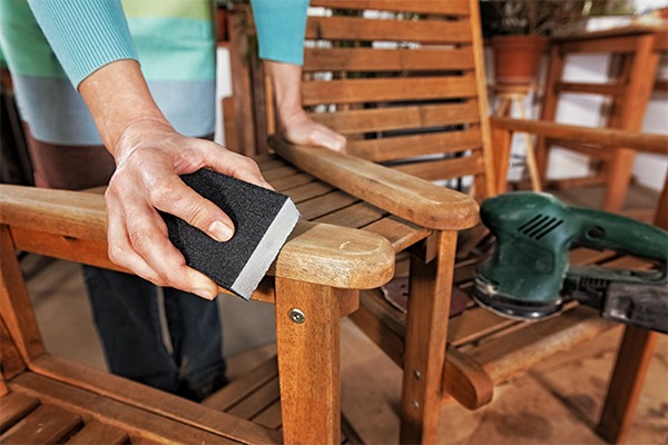 Person sanding a wooden chair with a sanding block.