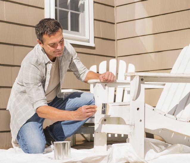 A man in casual clothes paints a white wooden outdoor chair.