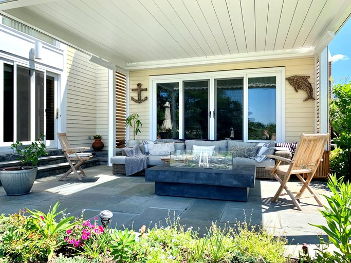 Outdoor patio with cushioned seating, wooden chairs, potted plants, and nautical decor.