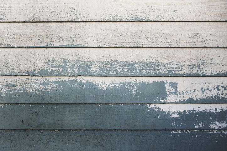 Weathered weatherboard wall with peeling blue and white paint, revealing natural wood texture beneath.