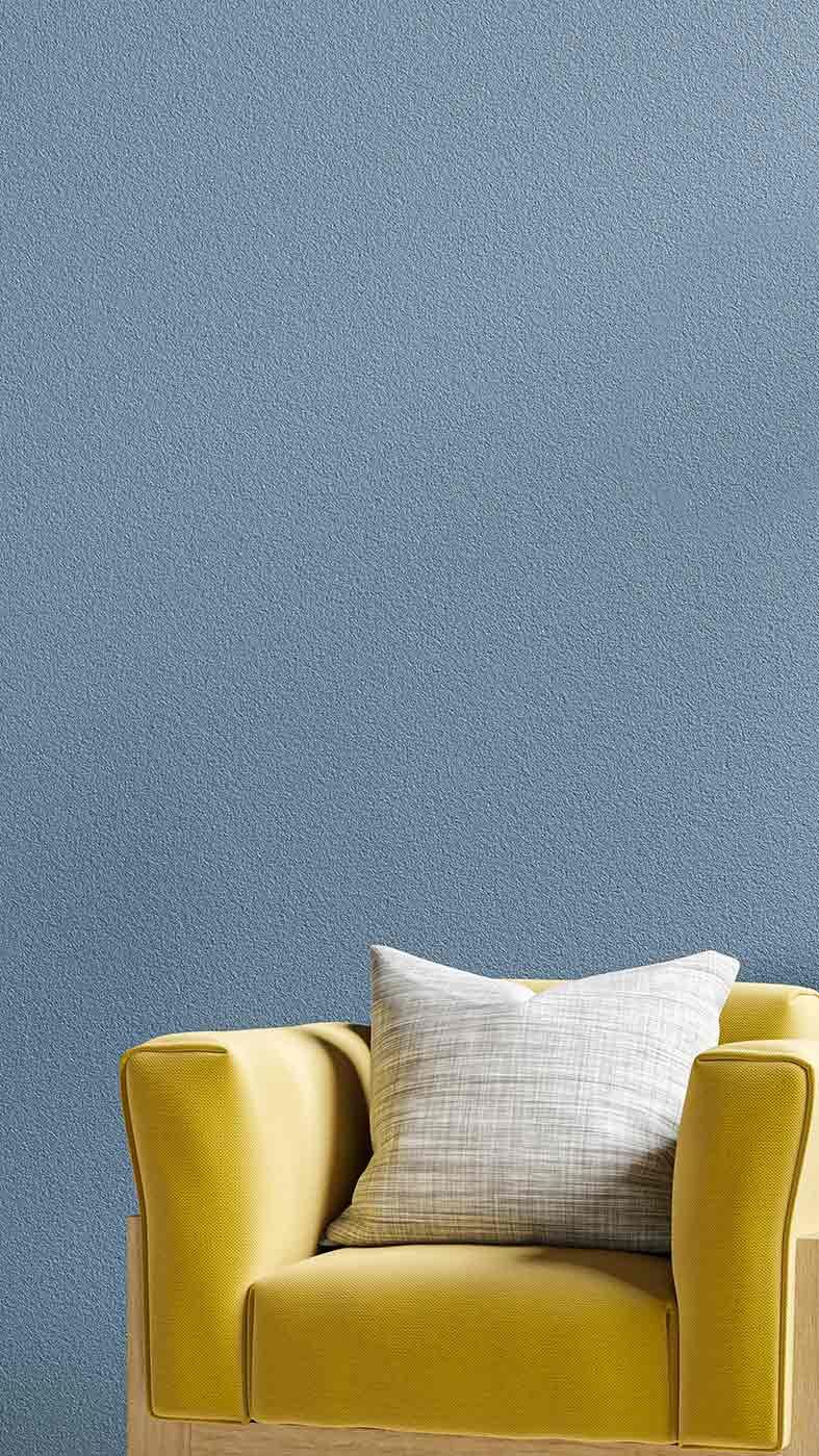 Yellow armchair with a light gray pillow against a textured blue-gray wall.